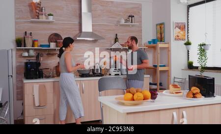 Cheerful married couple preparing breakfast and chatting. Husband having a conversation with wife while she is preparing eggs for breakfast. Stock Photo