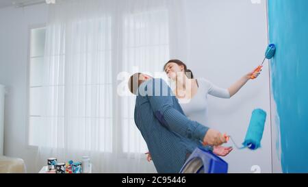 Cheerful young couple decorating apartment and dancing. Having fun and painting the walls. Apartment redecoration and home construction while renovating and improving. Repair and decorating. Stock Photo