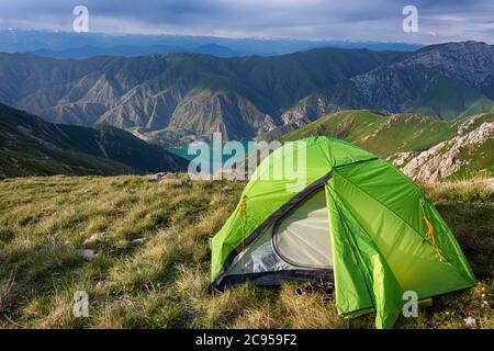 Idyllic summer landscape with hiking trail in the mountains with beautiful green tent, mountain pastures, lake, blue sky and clouds. Tian-Shan, Kyrgyz Stock Photo