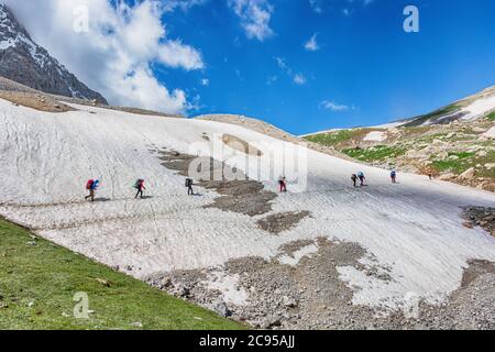 Idyllic summer landscape with hiking trail in snow mountains with trekkers, green mountain pastures, blue sky and clouds. Tian-Shan, Kyrgyzstan. Stock Photo
