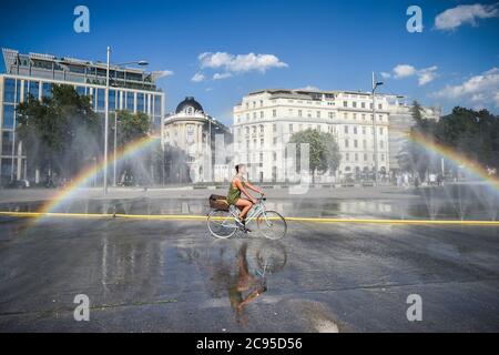 Beijing, Austria. 28th July, 2020. A cyclist passes a water spray on Schwarzenbergplatz in Vienna, Austria, July 28, 2020. The highest temperature in Vienna reached 37.2 degrees Celsius on Tuesday. Credit: Guo Chen/Xinhua/Alamy Live News Stock Photo