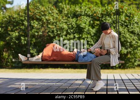 Young woman lying on her girlfriend's knees while they spending time on swing outdoors Stock Photo