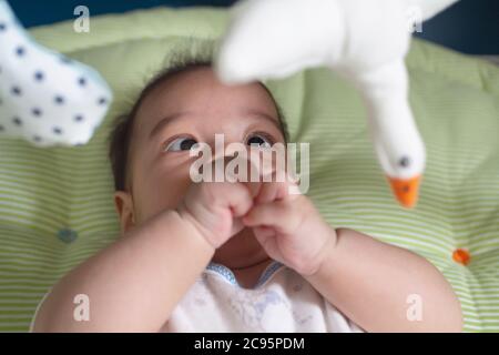 asian cute innocent baby newborn boy looking and play at the mobile hanging toy on the fabric crib after waking up in the morning. family, healthy and Stock Photo
