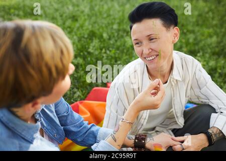 Two happy women sitting on the green grass and smiling they have picnic in the park Stock Photo