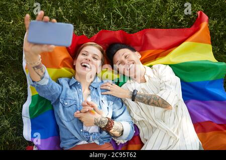High angle view of two lesbians lying on colored flag and making selfie portrait on mobile phone outdoors Stock Photo