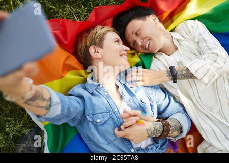 High angle view of two lesbians having fun making selfie portrait while lying on the grass Stock Photo