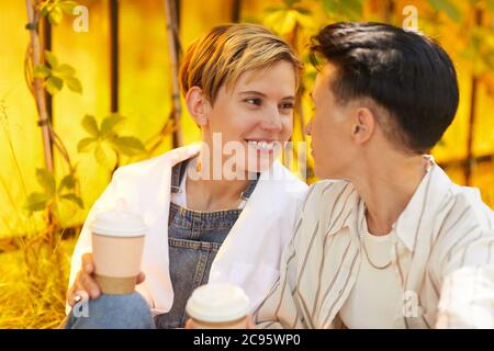 Young woman drinking coffee and talking to her girlfriend while they sitting outdoors Stock Photo