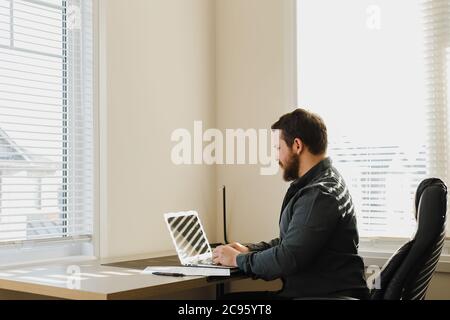 Male web developer sitting at desk and using laptop at cabinet. Stock Photo