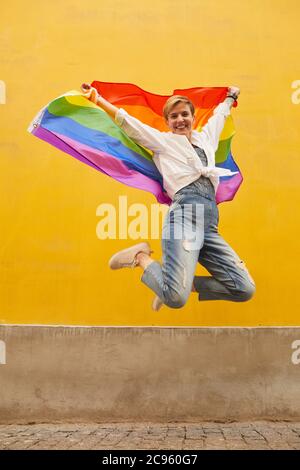 Portrait of young happy woman with colored flag smiling at camera and jumping outdoors Stock Photo