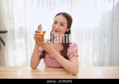 Profile of young elegant woman is sitting backstage and spraying perfume aside with closed eyes. She is recording video for her beauty blog using came Stock Photo