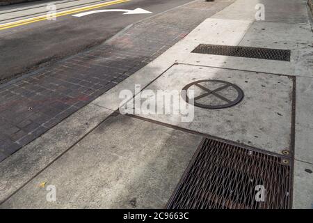 Dirty concrete and brick sidewalk alongside a street, turn lane arrow and streetcar rails, metal grate and manhole, Georgia USA, horizontal aspect Stock Photo
