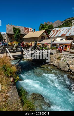 Wooden bridge over the Guisane river, and old houses in the small village of Le Casset, Serre Chevalier, near Briancon, Ecrins, France Stock Photo