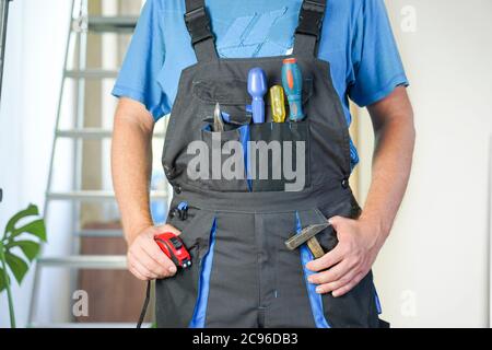 worker in overalls with tools stands against the background of repair Stock Photo