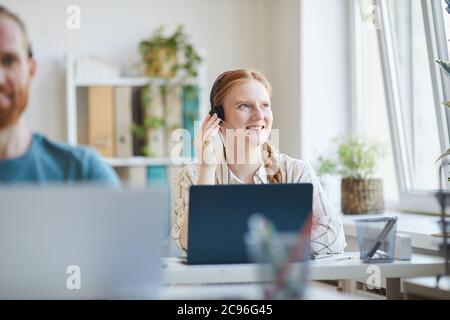 Young woman in headphones sitting at the table with laptop she working in call center Stock Photo