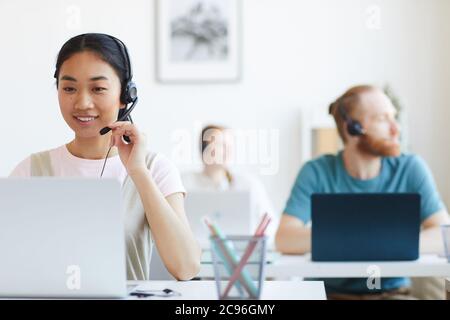 Asian smiling operator in headset working at her workplace at office Stock Photo