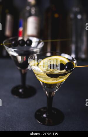 Alcohol cocktail with splash.Dry martini with black olives.Vermouth cocktail inside martini glass over dark background.Martini glasses are on the bar.