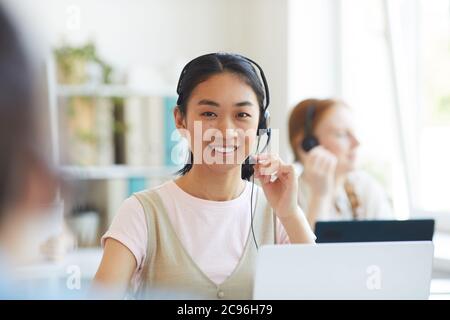 Portrait of Asian operator in headset smiling at camera while working in call center Stock Photo