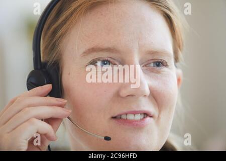 Close-up of red haired woman in headset working with clients at office Stock Photo