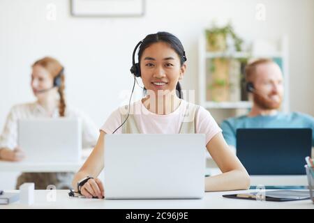 Asian young woman working in call centre, surrounded by colleagues Stock Photo