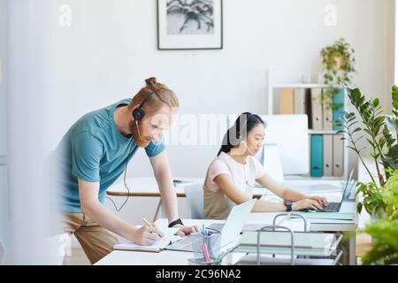 Call center agent in headphones making notes in note pad while taking the order at office Stock Photo