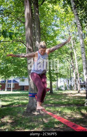 Sorel-Tracy, Canada-28 July 2020 : Smiling woman taking a break on a Base Line Slack Line recreational balance sport  in the park at summer Stock Photo