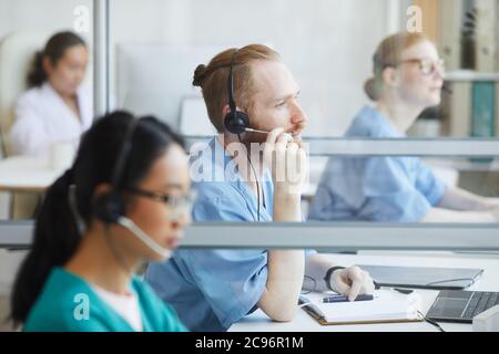Group of operators in headphones sitting at their workplaces and working in medical call center Stock Photo