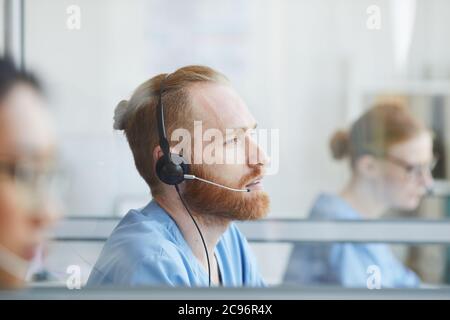 Young bearded man in headphones working in medical call center Stock Photo