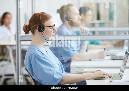 Operator in headset sitting at her workplace and typing on laptop computer she working in medical call center Stock Photo