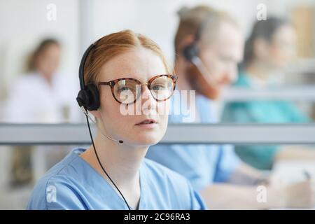 Close-up of young operator in eyeglasses and headset looking at camera while talking on the phone Stock Photo