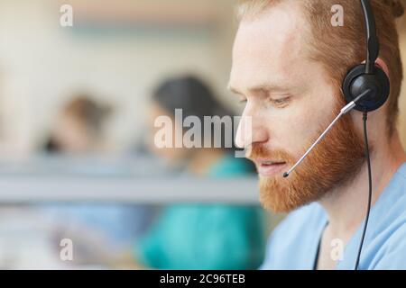 Close-up of bearded male operator using headset to talk to clients during his work in call center Stock Photo