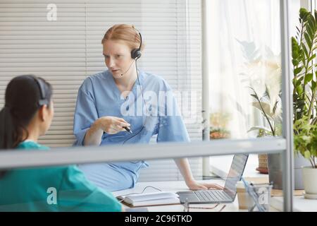 Two colleagues in headphones talking to each other during their work in medical call center Stock Photo