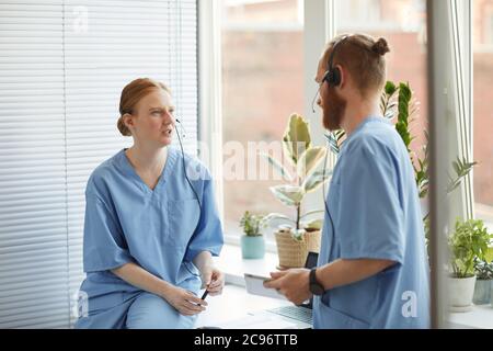 Two medical workers in uniform and headphones standing at office and discussing work together Stock Photo