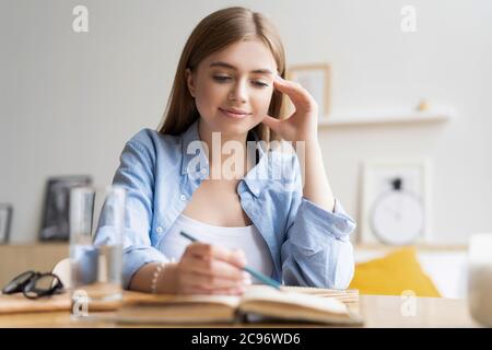 Focused young woman writing letter on table at home office. Concentrated businesswoman making notes in notebook Stock Photo