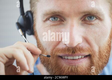 Close-up of bearded male operator in headphones smiling at camera and talking on the phone Stock Photo