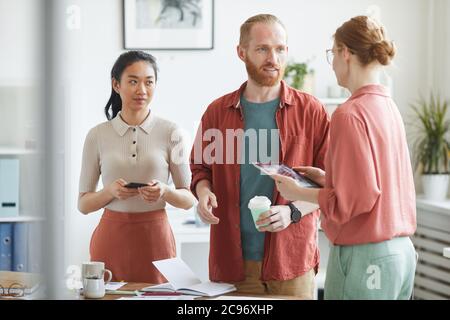 Group of business people talking to their colleague while she using digital tablet they standing at office Stock Photo
