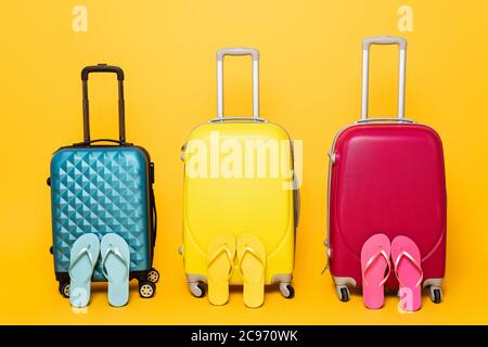 yellow, pink and blue travel bags with flip flops isolated on yellow Stock Photo