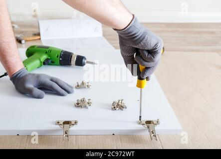 Furniture assembly using screwdriver. Male hands in gray gloves master collects furniture using screwdriver tools, instrument at home. Moving, home Stock Photo