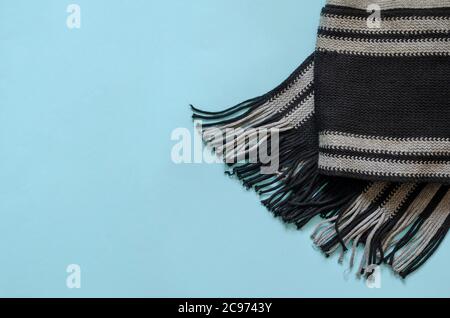 Gray woolen scarf on light blue background. Warm autumn clothing accessory. Top view at an angle. Coating space. Stock Photo