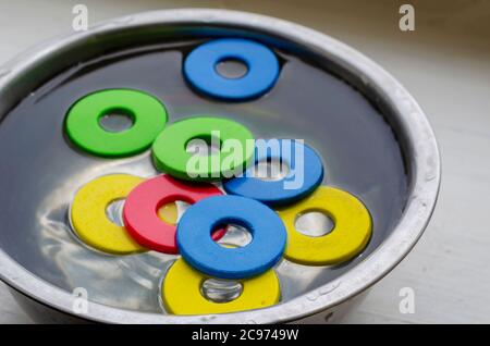 Multi-colored details of children's designer set in metal bowl with water. Cleaning children's toys from dirt and dust. Hygiene, health care. Selectiv Stock Photo