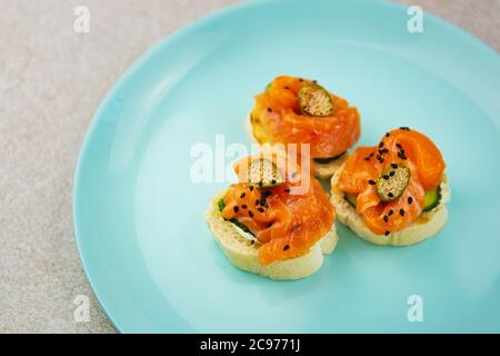 Canape snacks with red salmon fish fillet & capers served on blue ceramic plate for dinner.Delicious snack food cooked with natural seafood ingredient Stock Photo