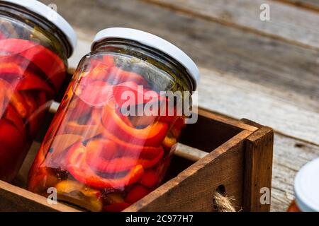 Wooden crate with glass jars with pickled red bell peppers.Preserved food concept, canned vegetables isolated in a rustic composition. Stock Photo