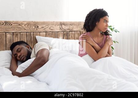Annoyed black girl sitting next to snoring boyfriend Stock Photo