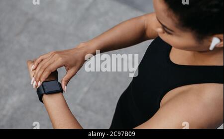 Running and heart rate. Woman checks fitness tracker on arm, jogging with wireless headphones Stock Photo