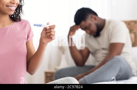 Happy woman with pregnancy test and upset man in bedroom Stock Photo