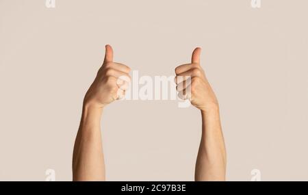 Unrecognizable man showing thumbs up gesture, expressing approval over light background Stock Photo