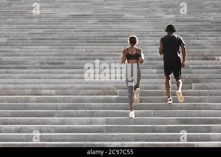 Outdoor sport. Black couple running on stairs in city park, rear view Stock Photo