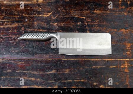 Shiny stainless steel meat cleaver with sharp blade lying on a rustic wooden board with copyspace viewed as a flat lay still life Stock Photo