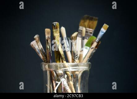 Collection of used and stained paintbrushes in an old glass jar over a dark background with copy space in a concept of art and creativity Stock Photo