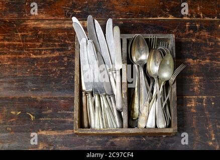 Collection of old vintage cutlery in a wooden tray with assorted silver spoons, knives and forks in an overhead view on an old rustic wooden board Stock Photo