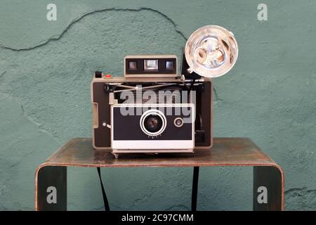 Old vintage instant camera with bellows and lamp on a small shelf in front of a damaged green textured wall in a photographic concept Stock Photo